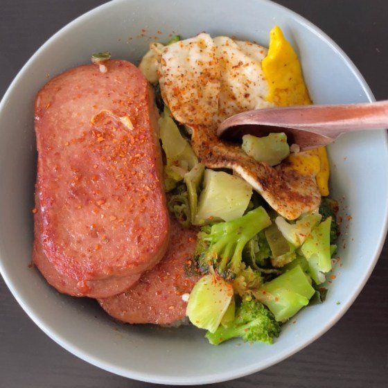 picture of a light blue bowl with spam with rice and broccoli on a black wood background